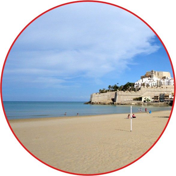 Strand mit feinem Sand, sanften Wellen und einer malerischen Klippenlandschaft im Hintergrund.